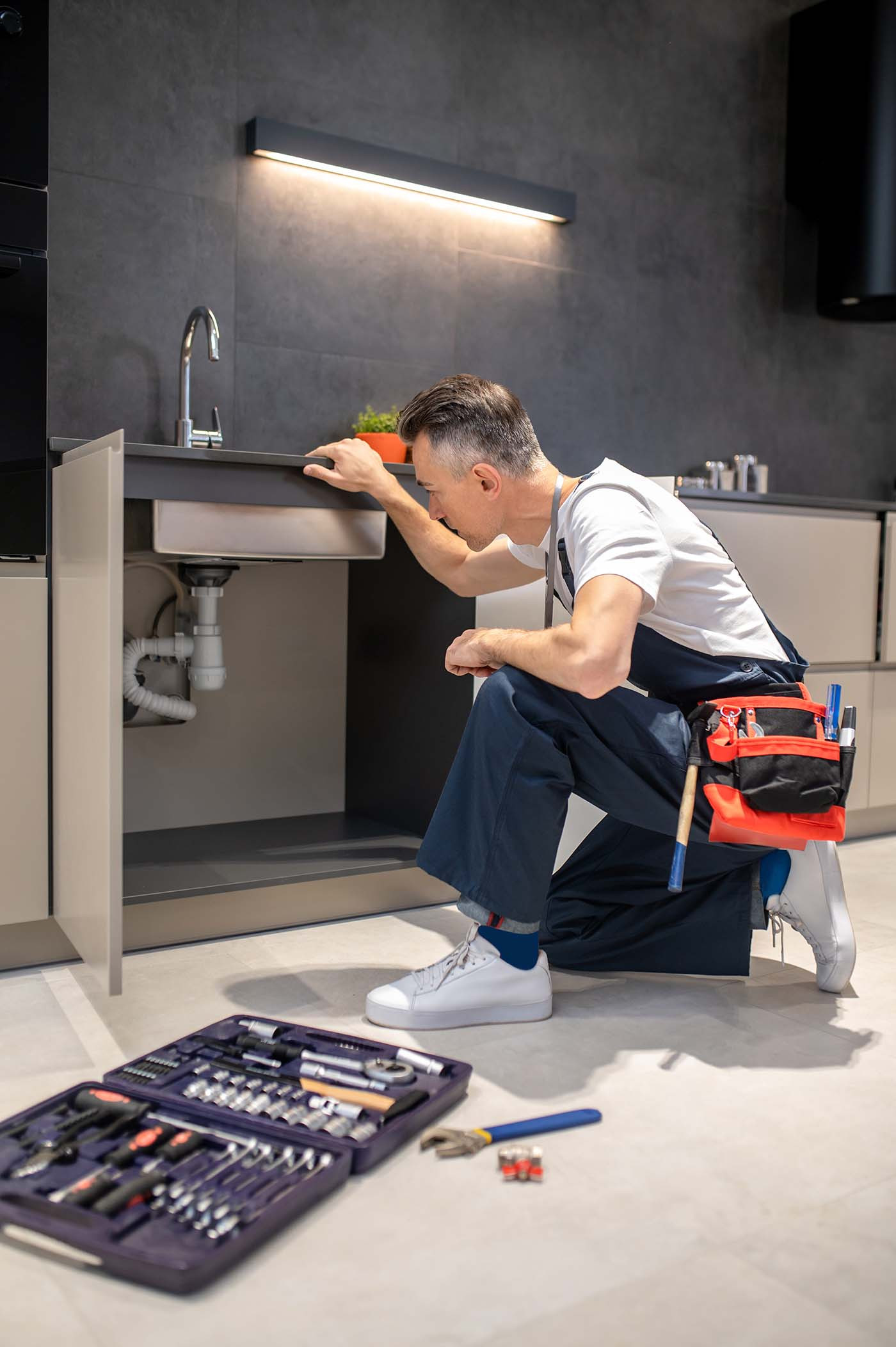Man kneeling down touching sink inspecting pipes 2023 11 27 05 20 45 utc